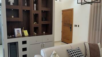 A modern living room with a white sofa, a wooden entertainment unit, and a hanging light fixture.