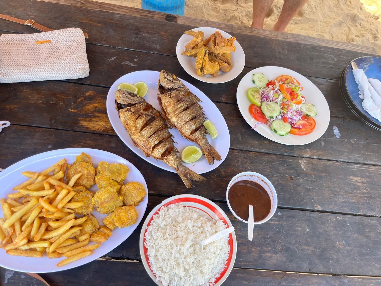 Un tavolo di legno con piatti di pesce fritto, patatine, riso e un'insalata.