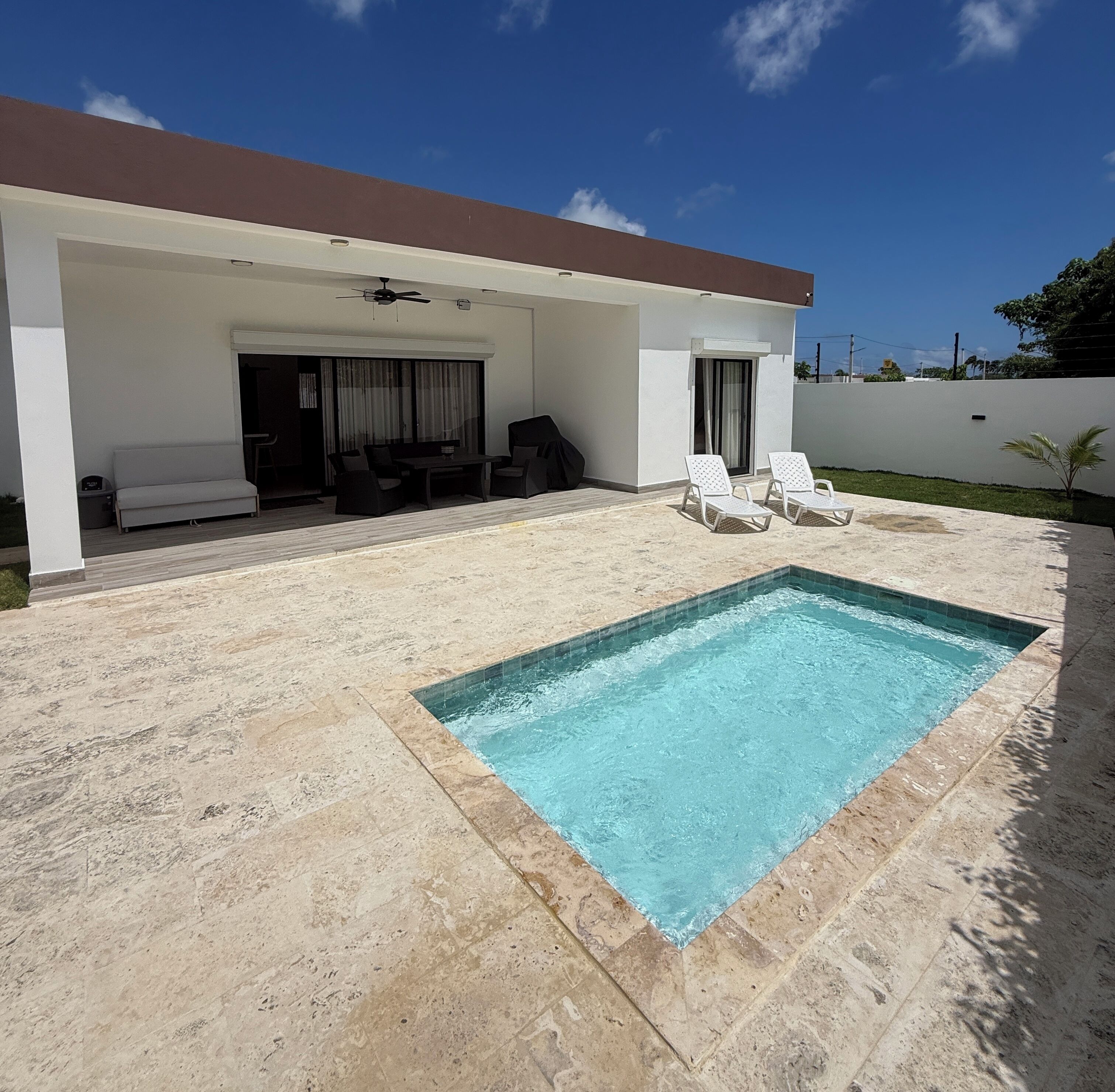 A covered outdoor area with a swimming pool, seating, and a ceiling fan.
