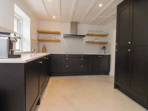 A kitchen with dark cabinets, a white countertop, and wooden shelves. - Rose Tree Cottage, Skipton (Skipton)