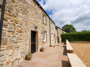 A stone building with a paved courtyard, a bench, and a potted plant. - Rose Tree Cottage, Skipton (Skipton)
