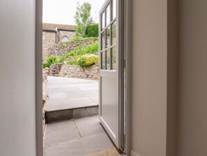 A doorway leading to a stone pathway and a stone wall with greenery. - Rose Tree Cottage, Skipton (Skipton)