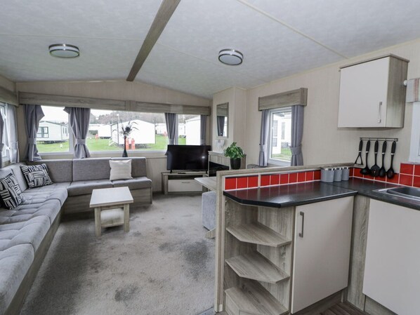A compact RV interior with a living area, kitchenette, and a view of the outside.