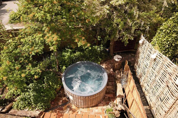 A hot tub surrounded by dense foliage, a wooden fence, and a brick pathway.