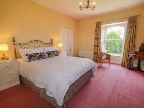 A bedroom with a bed, bedside lamps, a desk, a chair, and a window with curtains.