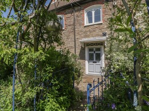 A stone house with a white door and window, surrounded by greenery and a blue metal fence. - Cefn Campstone, Abergavenny (Abergavenny)