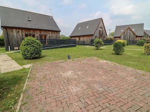 Une cour dallée de briques, avec des bâtiments en bois et de petits arbustes.
