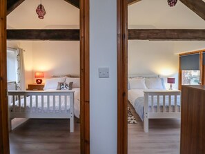 Ein Schlafzimmer mit zwei Betten, Holzbalken, einer weißen Wand und einer Pendelleuchte.