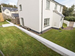 Una casa a due piani color bianco, con un piccolo giardino antistante e una recinzione in legno.