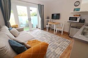 A modern room with a sofa, a small dining table, a TV, and a kitchen area with a microwave. - Blake Lodge, Crantock (Newquay)