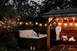 Un jacuzzi con estructura de madera, rodeado de follaje y luces colgantes.