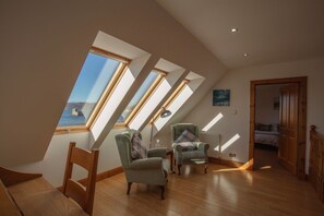 A room with a sloped ceiling, skylights, two armchairs, a wooden table, and a view of the outdoors.