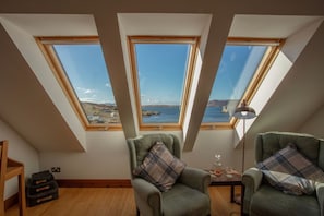 A room with two skylights, a view of the sea, and two green armchairs.