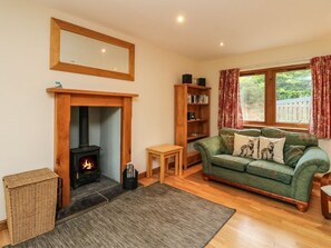 A cozy living room with a fireplace, a green sofa, a bookshelf, and a window with curtains. - Shepherds Rest nr Fort William (Fort William)