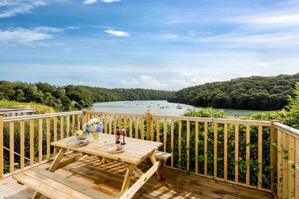 A wooden deck with a table set for dining, overlooking a lake with boats. - Fal River Cottage, Malpas, Cornwall (Truro)