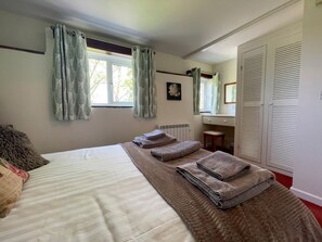 Ein Schlafzimmer mit Bett, Heizkörper, Fenster mit Vorhängen, Spiegel und Kleiderschrank.