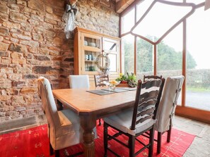 A dining area with a wooden table, leather chairs, a red rug, a stone wall, and a view through large windows. - The Boot Room, Ribchester (Preston)