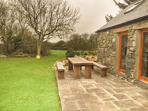 A stone building with a stone patio, a wooden bench, and a table. - Charming Bod Rhiw Retreat in Aberdaron (Pwllheli)