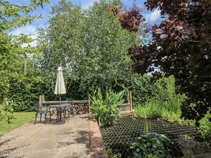 Une terrasse avec une table et des chaises, entourée de verdure et agrémentée d’un parterre de jardin délimité par un treillis métallique.
