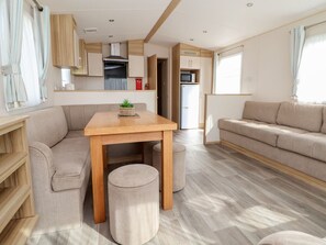 Interior moderno de autocaravana con una mesa de comedor de madera, sofá beige y una cocina con microondas y refrigerador.