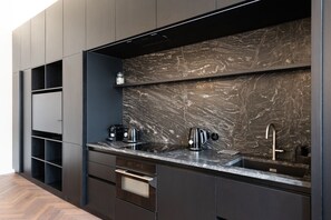 A modern kitchen with dark cabinetry, a marble backsplash, a built-in oven, and a sink with a faucet. - High-End 1BR Apt. with A/C & Parking Steps from Wenceslas Square by EasyBNB Premium (Prague)