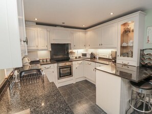 A modern kitchen with white cabinetry, granite countertops, a built-in oven, and a wine rack. - Manor Cottage, Cloughton (Scarborough)