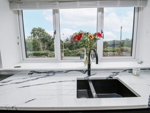 Eine Küche mit einer weißen Marmorarbeitsplatte, einem schwarzen Spülbecken und einem Fenster mit Blick auf Grünflächen.