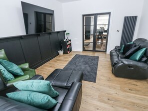 Ein modernes Wohnzimmer mit einem schwarzen Ledersofa, einem grünen Sessel und einer schwarzen Lederausklappsofa. Es gibt einen schwarzen Schrank, einen kleinen Tisch mit einer Lampe und eine Glastür, die in einen Essbereich führt.