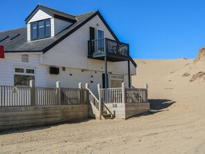 A white building with a balcony, a wooden fence, and a staircase leading to the entrance. - Charming Sandunes 2 Retreat in Camber (Rye)