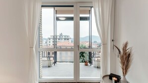 A room with a large sliding glass door leading to a balcony with a view of buildings and mountains. - Ruan Downtown - MyHomeinComo (Como)