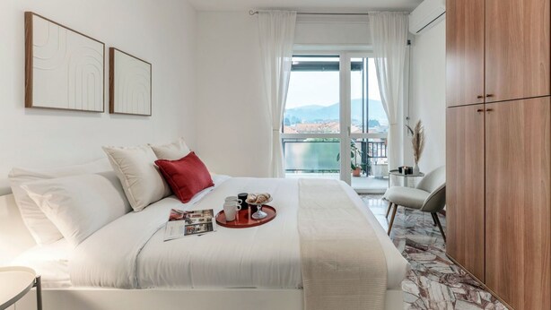 A hotel room with a bed, a side table, a chair, a wardrobe, and a window with a view. - Ruan Downtown - MyHomeinComo (Como)
