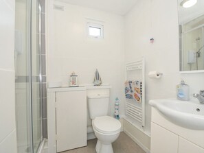 A bathroom with a glass shower enclosure, a toilet, a sink, and a towel rack. - 13 Hillside, Kilkhampton (Bude)