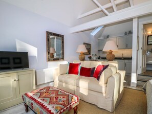 A living room with a sofa, a television, a patterned ottoman, a kitchen in the background, and a skylight. - The Garden Room in Chichester. (Chichester)