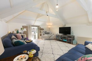 A cozy loft-style living room with a high ceiling, a television, and a fireplace. - Stable Loft, Watergate Bay (Newquay)