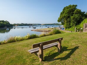 A wooden bench by a calm lake with boats, a grassy area, and a tree. - Joymead: Charming Retreat in Malborough (Kingsbridge)