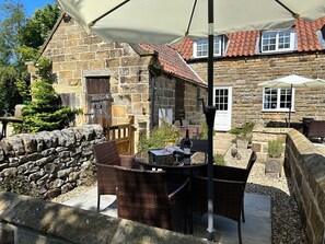 A stone building with a tiled roof, a stone wall, and a table with chairs under a canopy. - Charming Smugglers Rock Cottage (Scarborough)