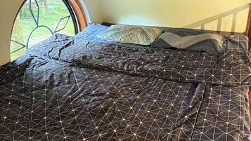 A bed with a geometric patterned bedspread, a window with a metal grill, and a corrugated metal ceiling.