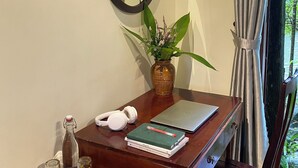 Un escritorio de madera con una computadora portátil, un espejo, una planta en maceta, una botella y un par de audífonos.