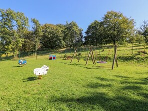A grassy outdoor area with a swing set, picnic table, and a blue toy car.
