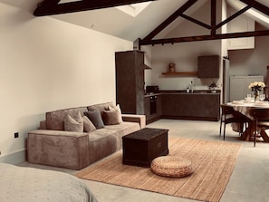 A modern living room with a sofa, ottoman, and rug, a kitchen with a dining area, and exposed wooden beams. - Charming Wabi in Gembling, Yorkshire (Driffield)