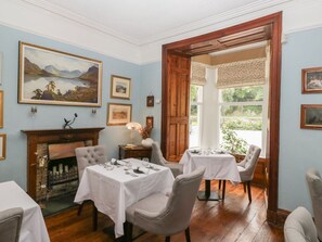 Ein Esszimmer mit zwei Tischen, einem Kamin und gerahmten Kunstwerken an den Wänden.
