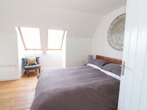 A bedroom with a large bed, two skylights, a chair, and a round wall decoration.