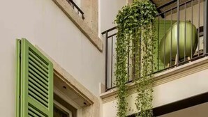 Un edificio con contraventanas verdes, un balcón con plantas y un arco de entrada.
