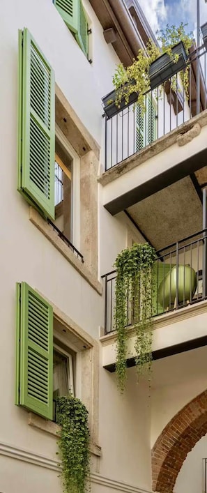 A building with green shutters, a balcony with plants, and an arched doorway. - Elegant apartment in the historic center of Verona (Verona)