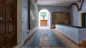 Un pasillo con una puerta de madera, un mapa enmarcado y vista de un edificio a través de un arco.