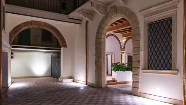 Un pasillo interior con arcos de piedra, suelo a cuadros y vista a otra habitación.