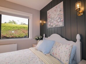 A bedroom with a bed, a window, a wall-mounted painting, and a wall sconce. - Charming Lake View House Apartment (Newry)