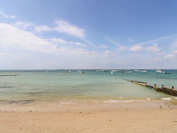 Una playa con aguas tranquilas y barcos anclados en la distancia.