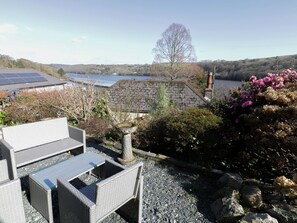 A patio with outdoor furniture, a stone table, and a view of a lake and hills. - Treetops: A Hidden Gem in Golant (Fowey)