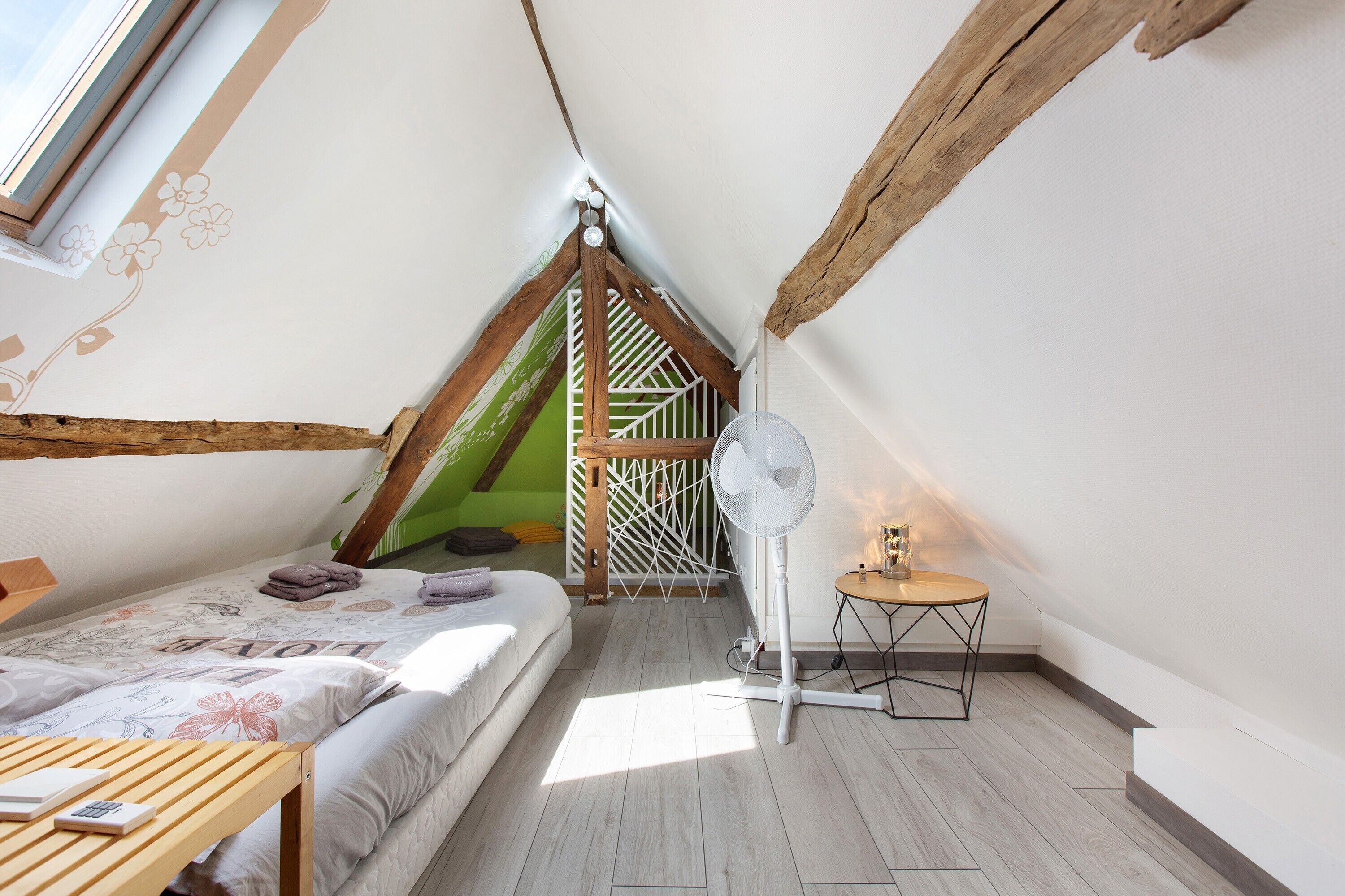 Une chambre avec un plafond en pente, un lit, une petite table, un ventilateur et un escalier menant à un niveau supérieur.